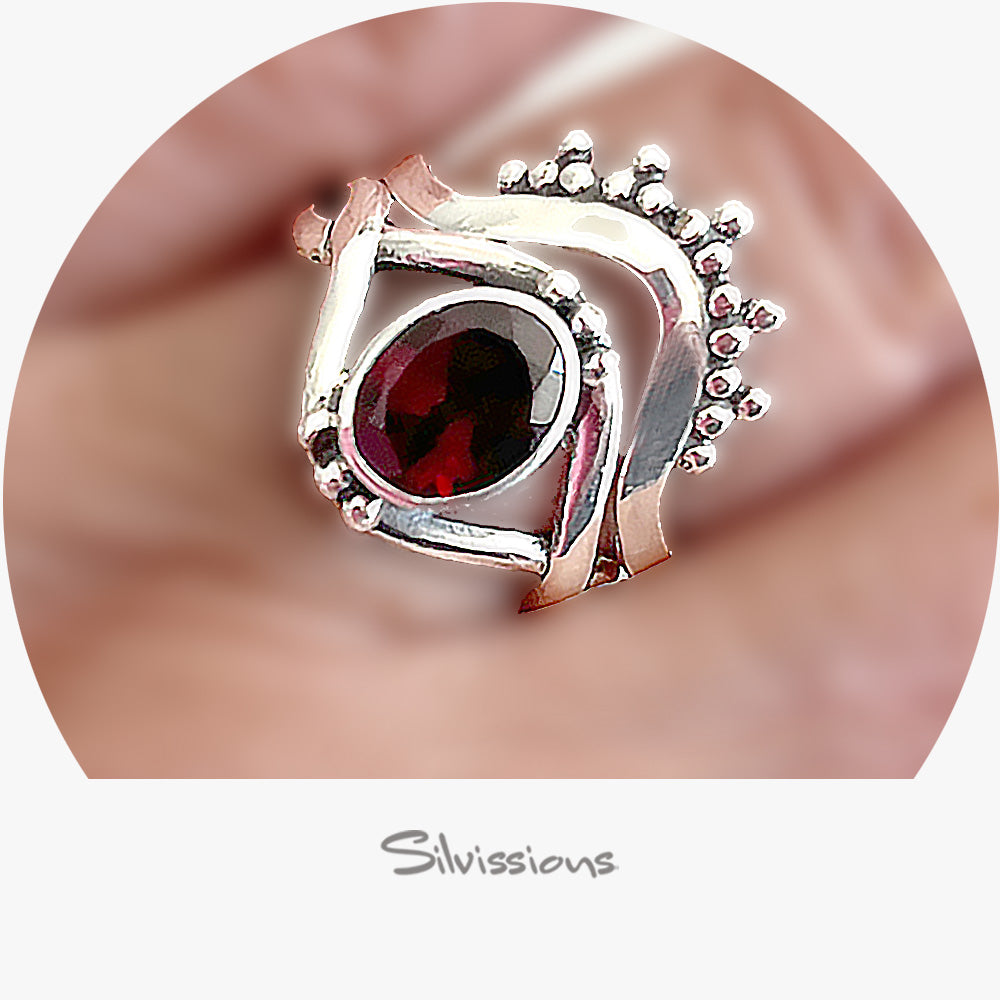 Silver ring with a red gemstone on a blurred background, featuring the brand 'Silvissions'.