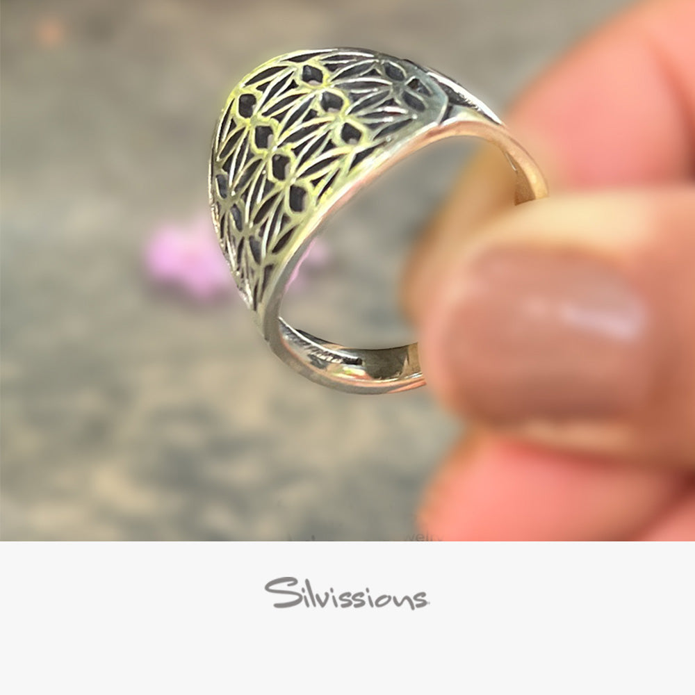 Silver ring with intricate design held by a hand, blurred background, Silvissions branding.
