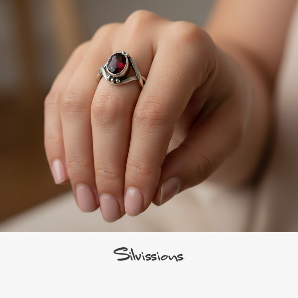 Hand wearing a silver ring with a red gemstone, blurred background, Silvissions brand visible
