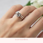 Silver knot ring on a hand with a blurred floral background, featuring the brand 'Silvissions'.