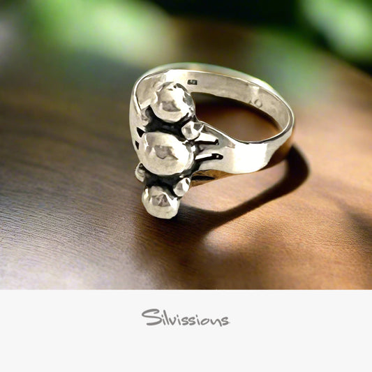 Silver ring with detailed design on a wooden surface, brand 'Silvissions' visible.