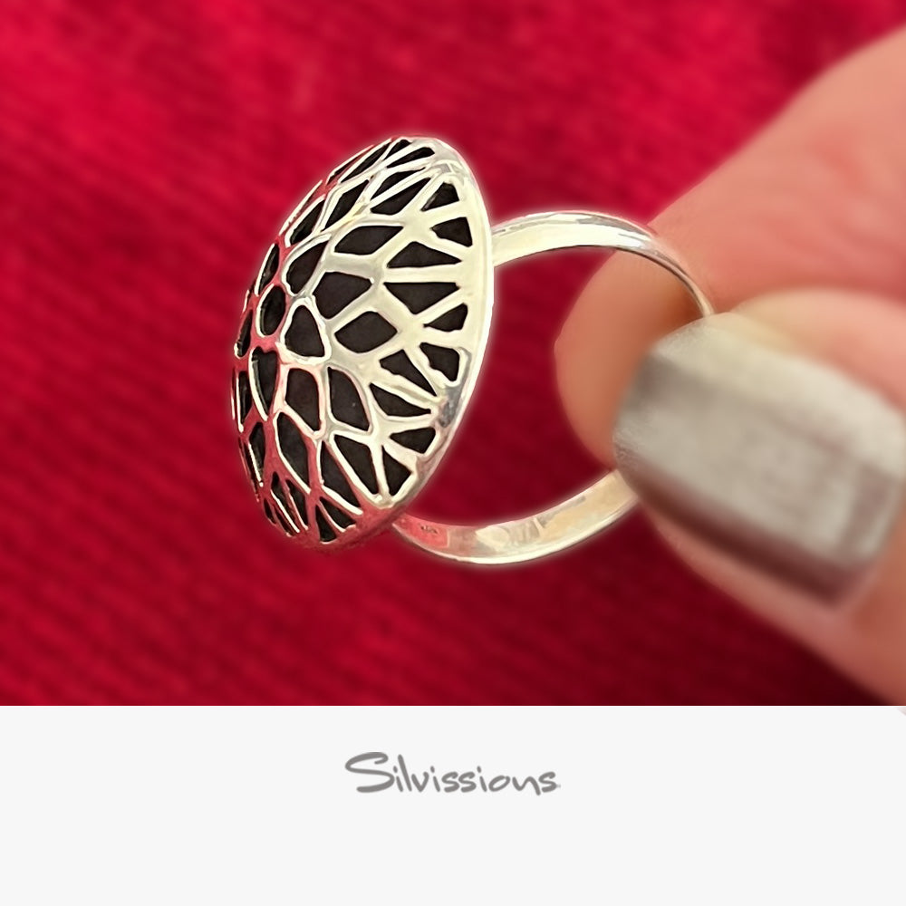 Silver ring with black geometric design held by a hand against a red background, featuring the brand 'Silvissions'.