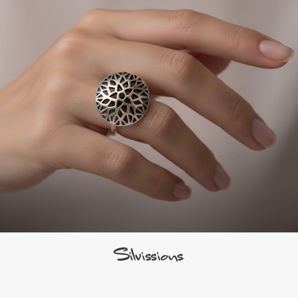 Silver ring with black geometric design held by a hand against a red background, featuring the brand 'Silvissions'.