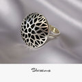 Silver ring with intricate design on a gray surface with white flowers in the background, featuring the brand 'Silvissions'.