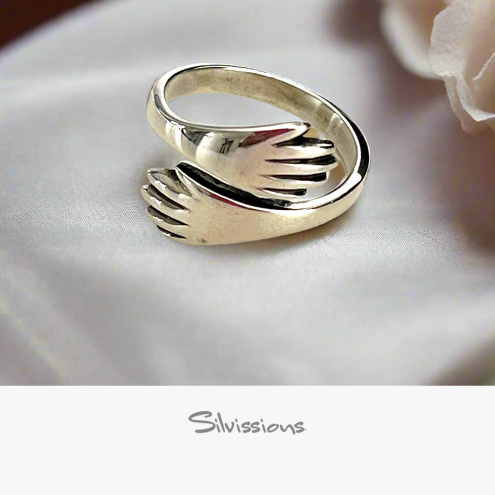 Silver ring with 2 hands design on a white fabric background, branded 'Silvissions'.