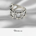 Silver ring with intricate family design on a light beige background, branded 'Silvissions'.