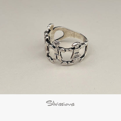 Silver ring with intricate family design on a light gray background, branded 'Silvissions'.