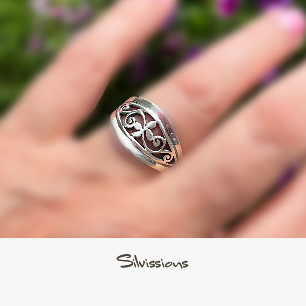 Silver ring with intricate design on a hand, blurred background with 'Silvissions' branding.