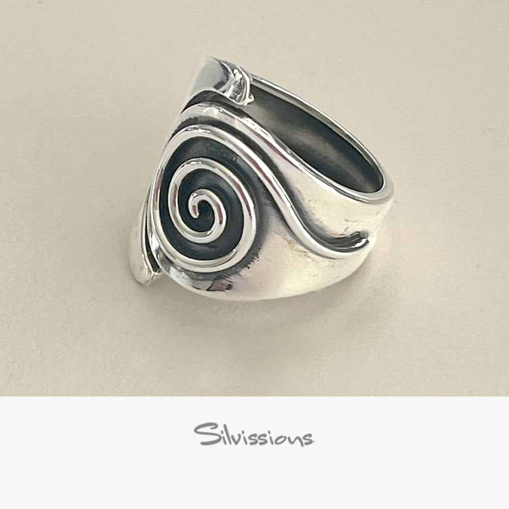 Silver ring with spiral design on a gray surface, featuring Silvissions Jewelry branding.