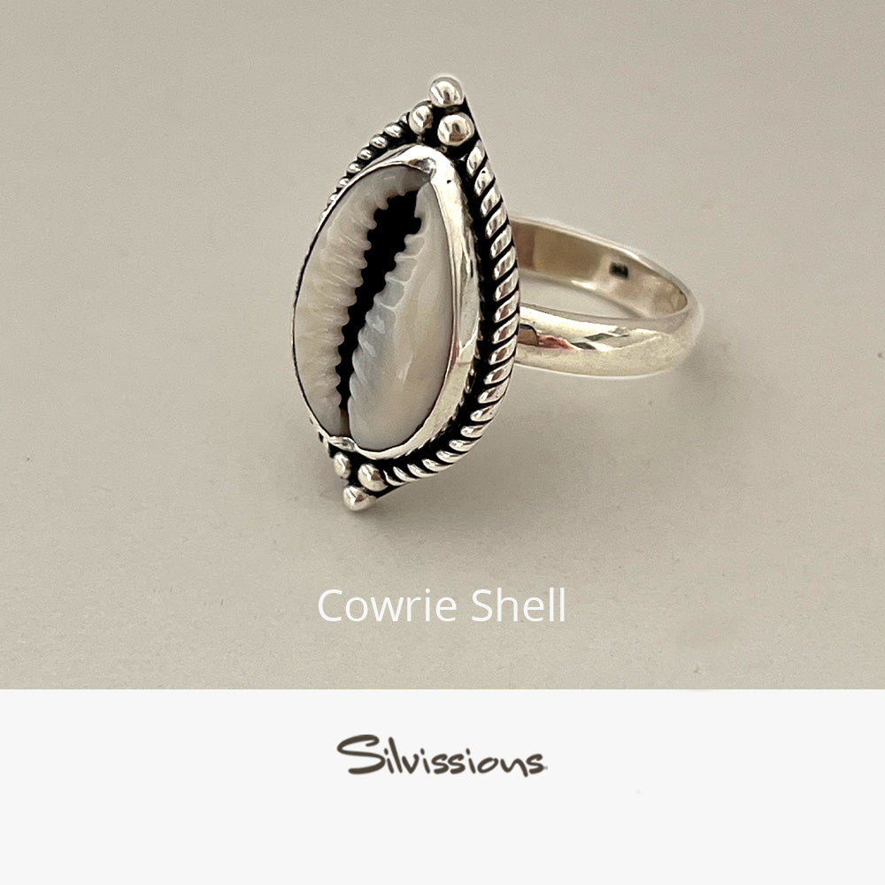 Silver ring with cowrie shell design on a beige background, featuring the brand 'Silvissions'.