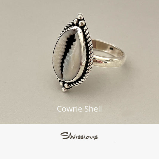 Silver ring with cowrie shell design on a beige background, featuring the brand 'Silvissions'.