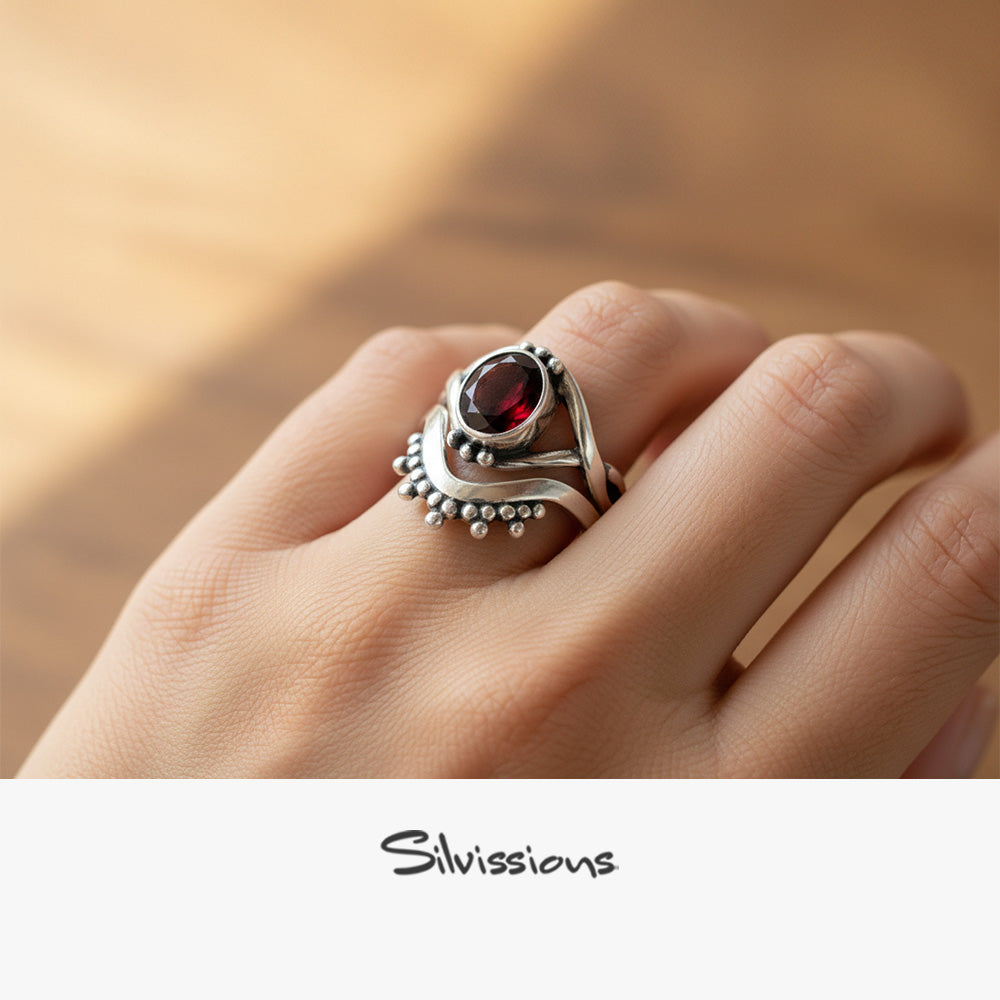 Silver ring with a red gemstone on a hand, branded 'Silvissions'.
