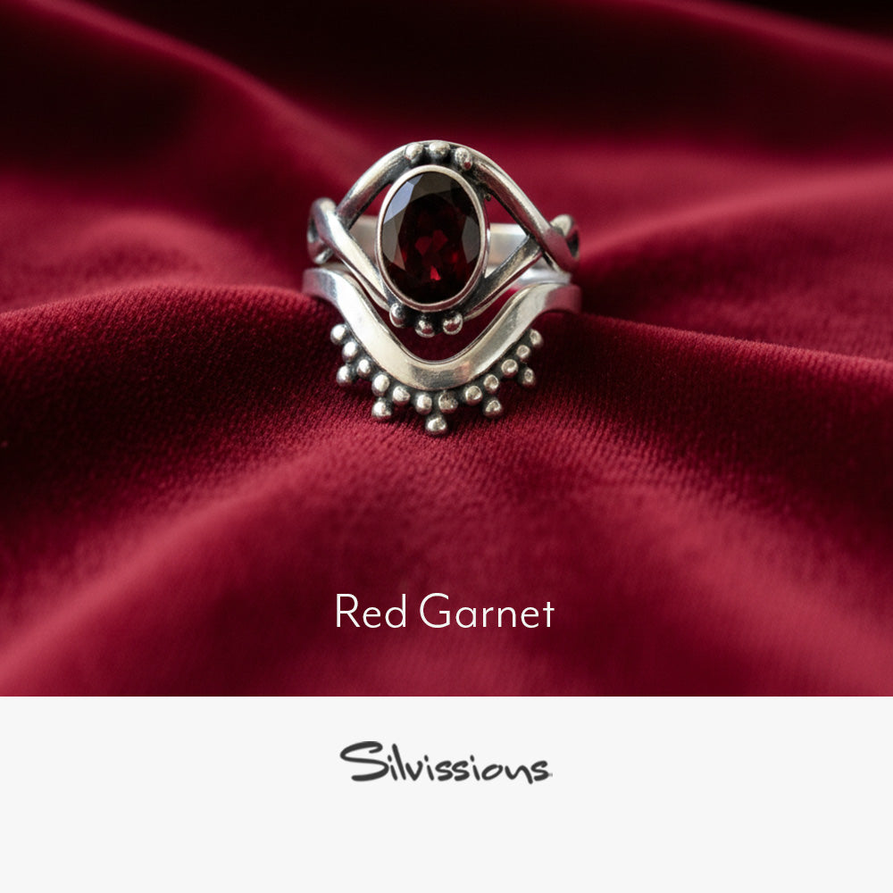 Silver ring with red gemstone on red fabric, branded 'Silvissions'.
