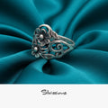 Silver floral ring on teal fabric with 'Silvissions' branding