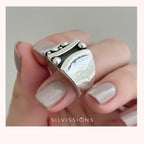 Silver ring with a textured design held by a hand with light nail polish on a neutral background, featuring the Silvissions brand.