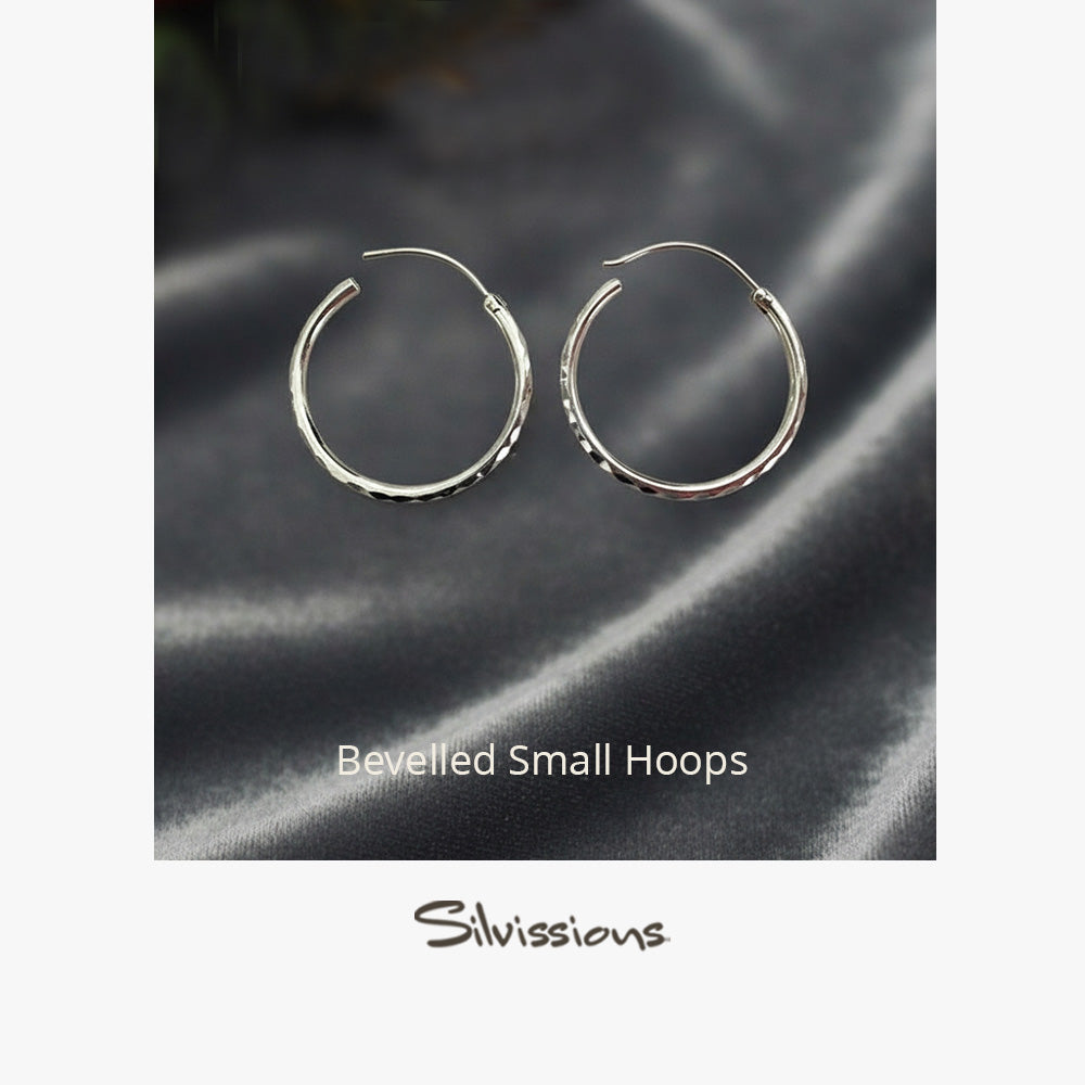 Silver hoop earrings on a dark fabric surface with a blurred background