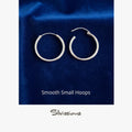 Pair of silver hoop earrings on a blue fabric background with 'Silvissions' branding.