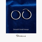 Pair of silver hoop earrings on a blue fabric background with 'Silvissions' branding.