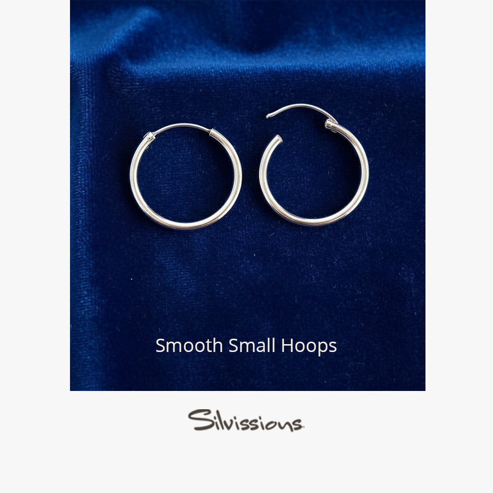 Pair of silver hoop earrings on a blue fabric background with 'Silvissions' branding.