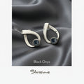 Pair of silver earrings with black onyx stones on a gray fabric background, featuring the brand 'Silvissions'.