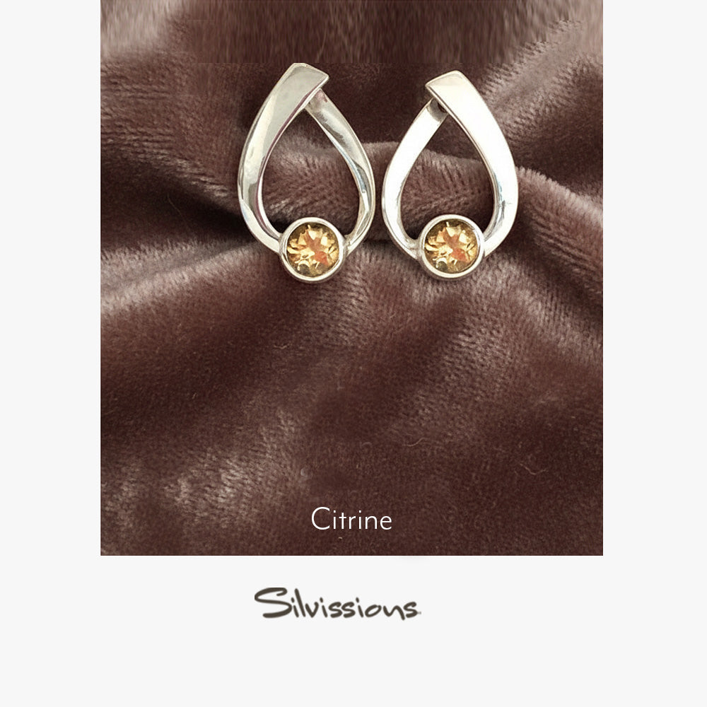 Silver earrings with citrine gemstones on a brown fabric background, featuring the Silvissions brand.