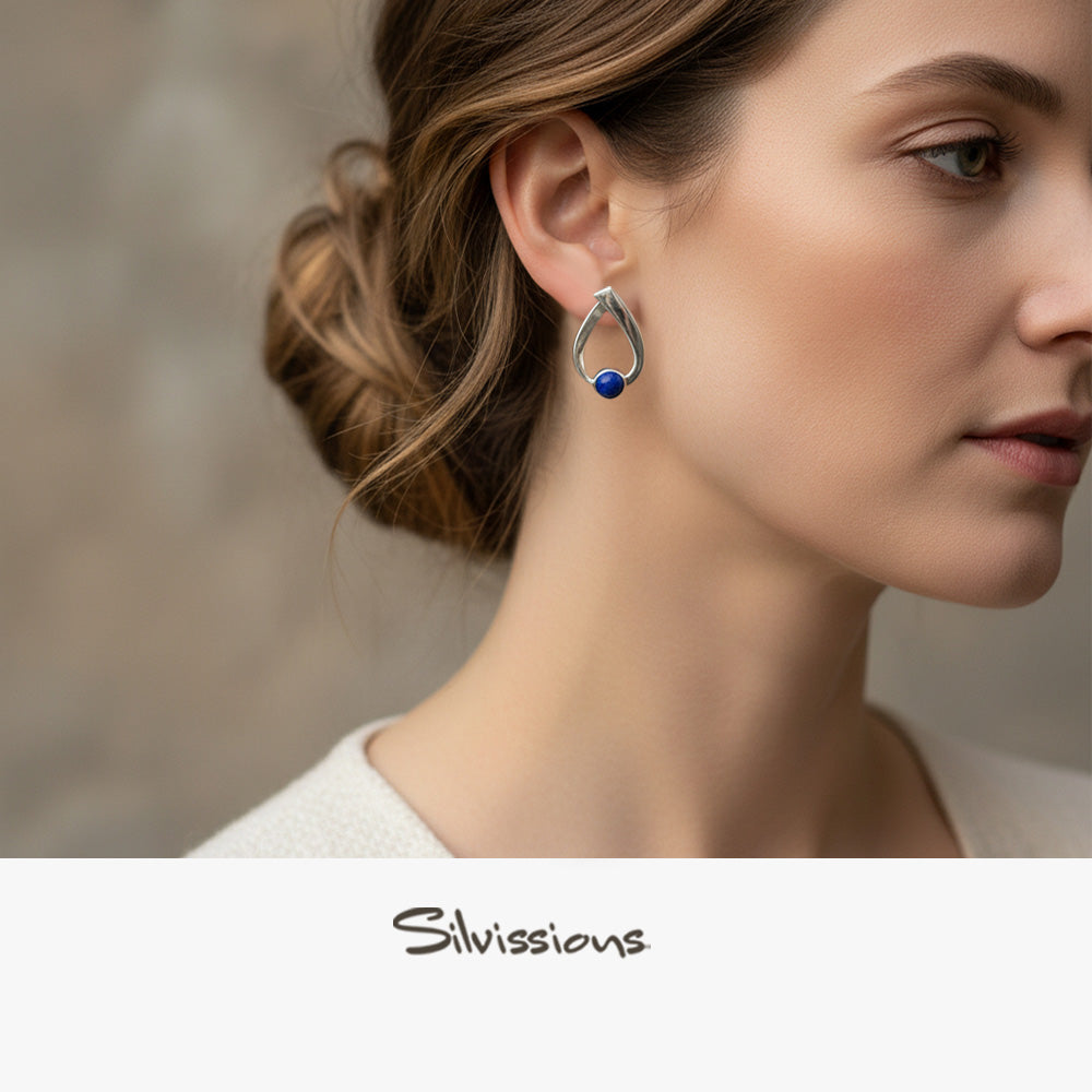 Close-up of a woman wearing a silver earring with a blue gemstone, branded 'Silvassions'.