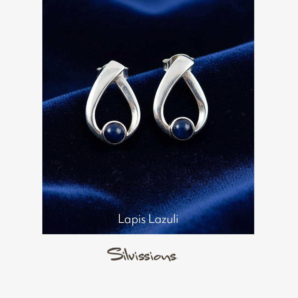 Silver earrings with blue gemstones on a dark blue fabric background, featuring the brand 'Silvissions'.