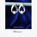 Pair of silver earrings with mother of pearl stones on a blue satin background, branded 'Silvissions'.