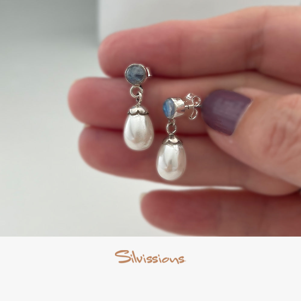 Silver earrings with pearls and blue gemstones held in a hand.