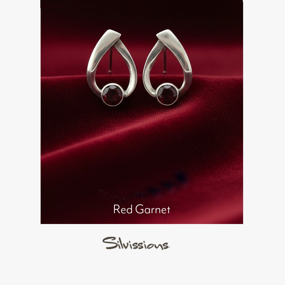 Silver earrings with red gemstones on a soft pink background, branded 'Silvissions'.