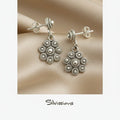 Silver floral earrings on a beige background with 'Silvissions' branding.