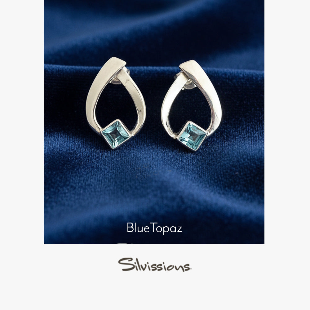 Silver earrings with blue gemstones on a dark blue fabric background, featuring the brand 'Silvissions'.