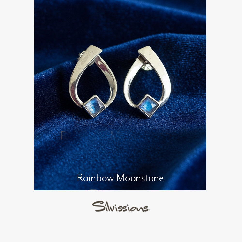 Silver earrings with blue stones on a blue fabric background, branded 'Silvissions'.
