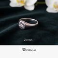 Silver ring with zircon stone on a dark fabric background with white orchids.