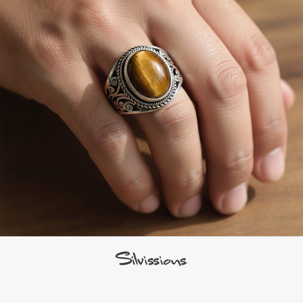 Close-up of a hand wearing a decorative ring with a tiger's eye stone on a wooden surface, branded 'Silvissions'.