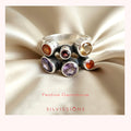 Silver ring with colorful gemstones on beige satin fabric, featuring the brand 'Silvissions'.