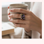 Hand holding a ceramic mug with colorful rings on the ring finger, blurred background