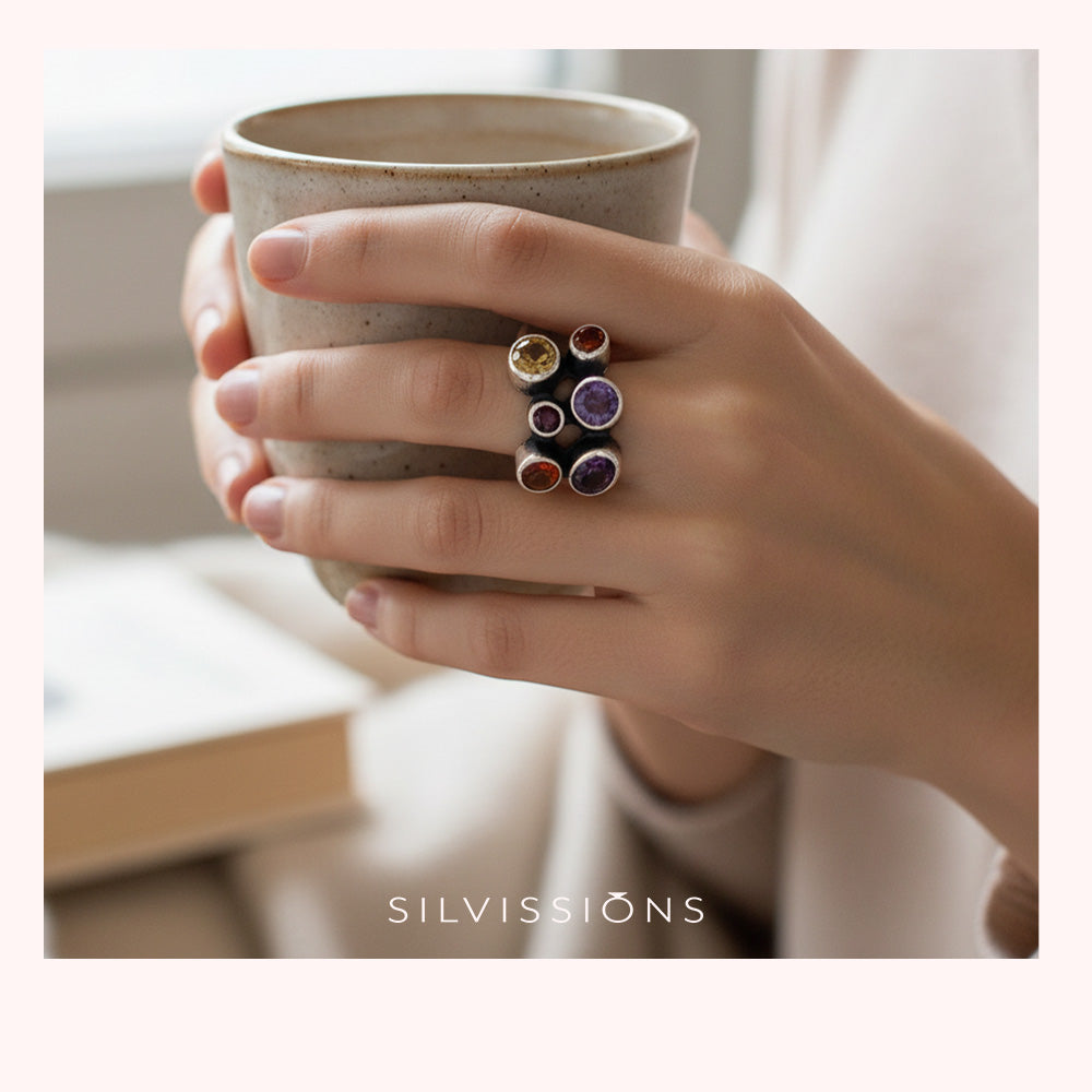 Hand holding a ceramic mug with colorful rings on the ring finger, blurred background
